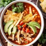 A bowl with chicken tortilla soup with avocado slices and cilantro.