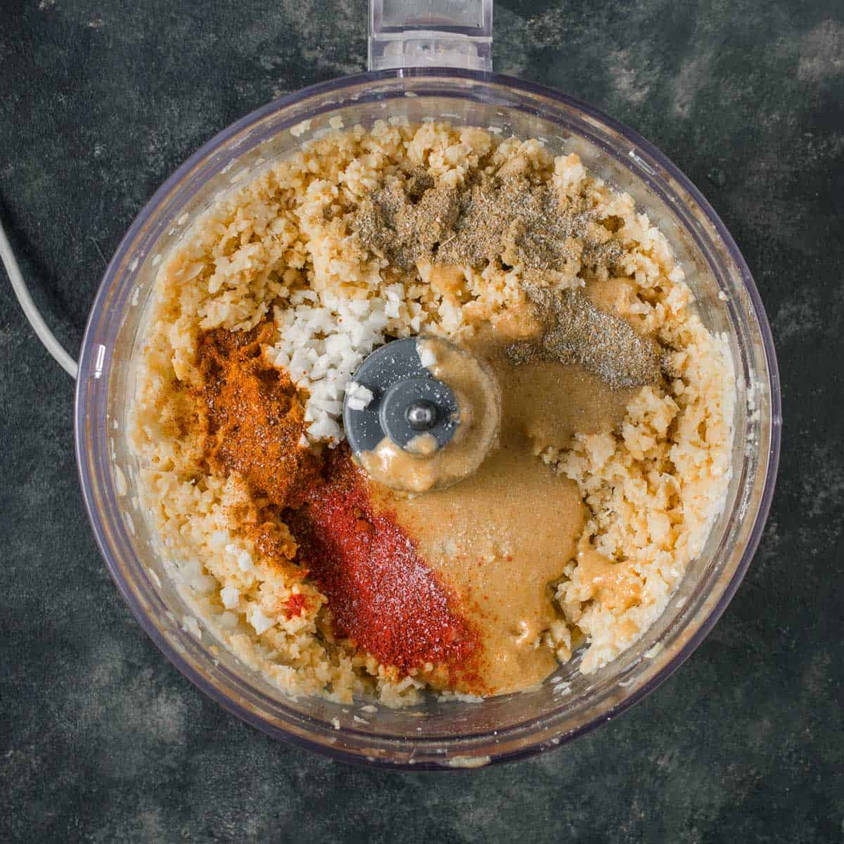 Adding spices to hummus in a food processor.