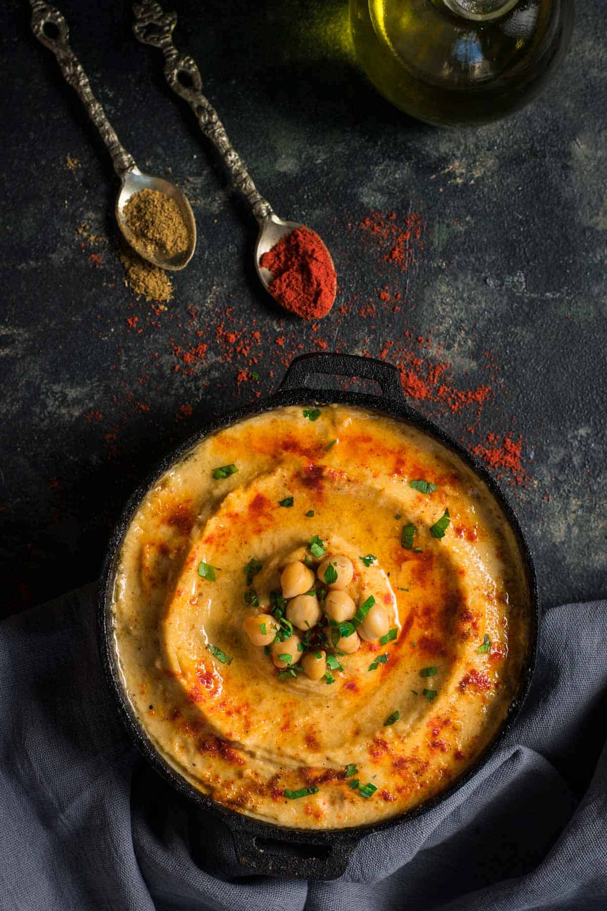 An overhead shot of a creamy hummus sprinkled with paprika and served with spoons.