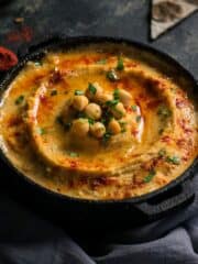Homemade garlic hummus dip topped with some whole chickpeas and sprinkled with paprika in a black dish.