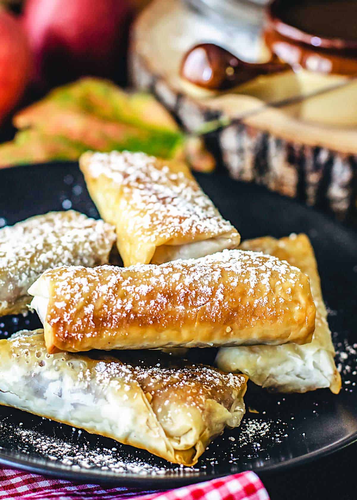 Golden fillo rolls filled with apple pie filling stacked on a plate.