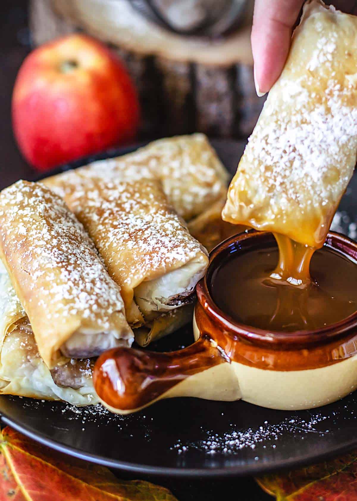 An apple pie filo roll dipped into a caramel sauce.