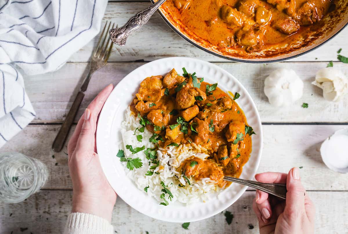 Vertical shot of the chicken tikka masala on a plate with rice and in a pan.