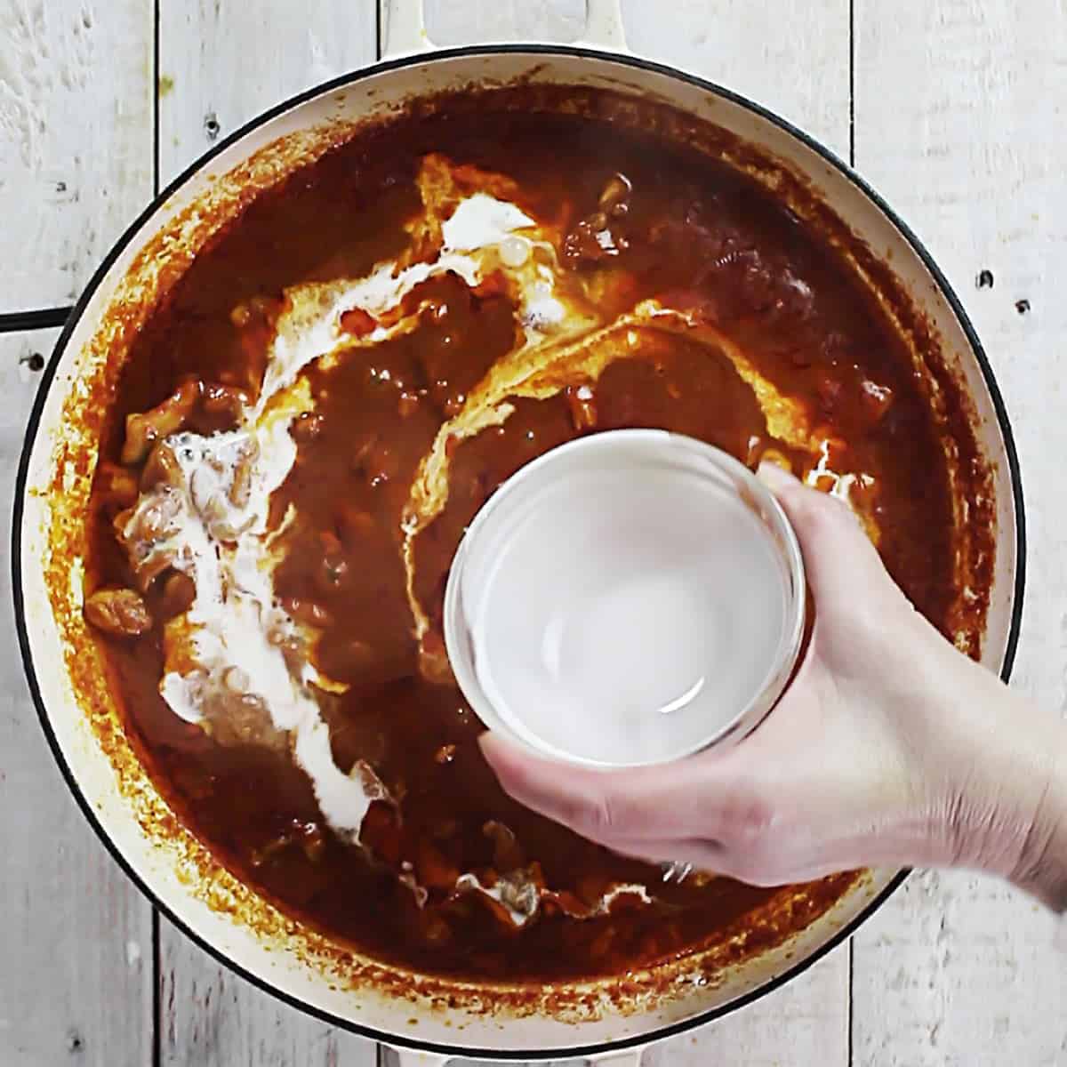 Process shot showing heavy cream being added to chicken tikka masala sauce.