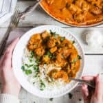 Chicken tikka masala with rice in a bowl and garnished with cilantro.