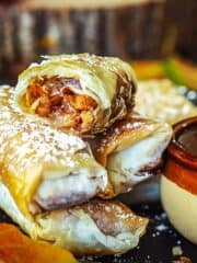 Stacked apple pie filo rolls with the top one being split in half to reveal the filling.
