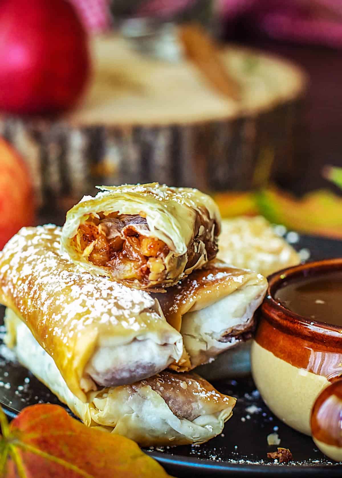 Stacked apple pie filo rolls with the top one being split in half to reveal the filling.