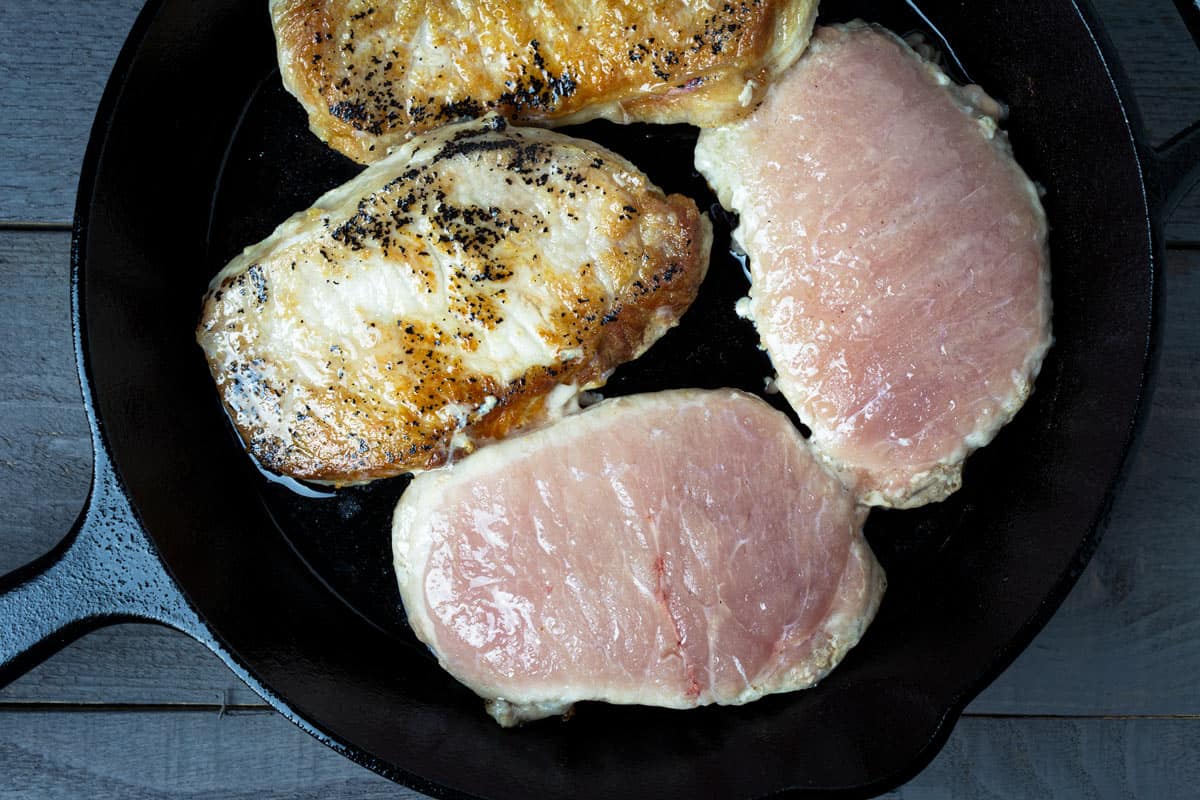 Searing the pork cutlets in a cast-iron skillet.