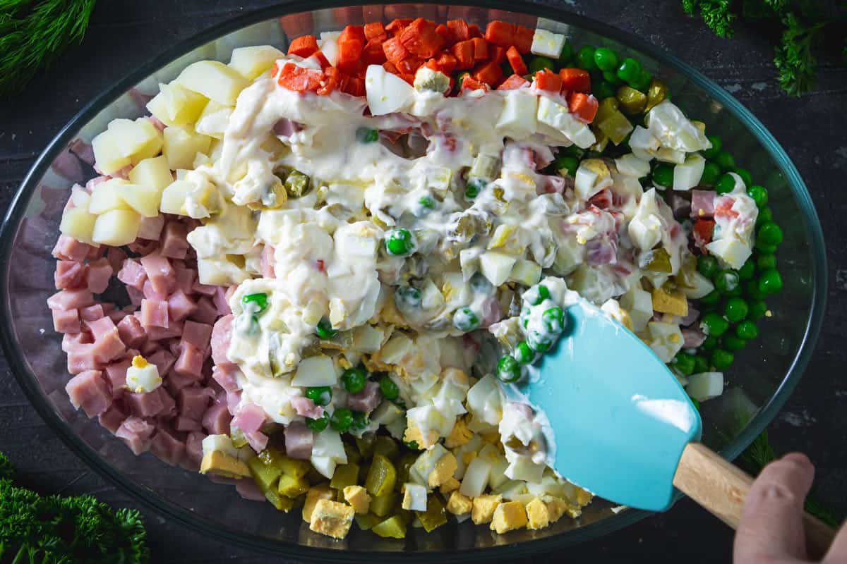 Mixing the Olivier salad ingredients to combine them.