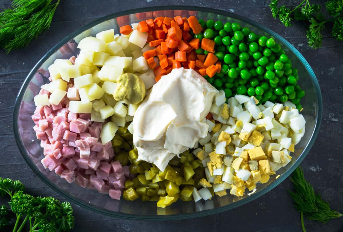Russian Olivier salad ingredients in an oval dish.