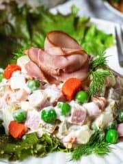 A close up of Russian potato salad served over a lettuce leaf and topped with a sliced ham "rose."