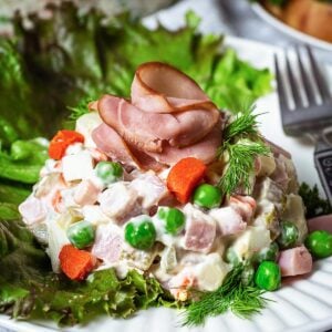 A close up of Russian potato salad served over a lettuce leaf and topped with a sliced ham "rose."